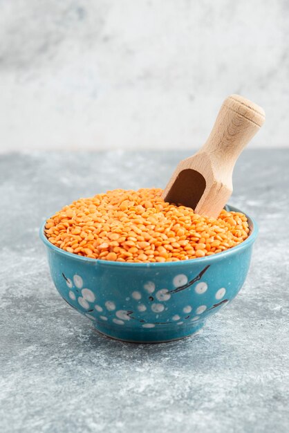 Blue bowl of raw red lentils on marble table with spoon.