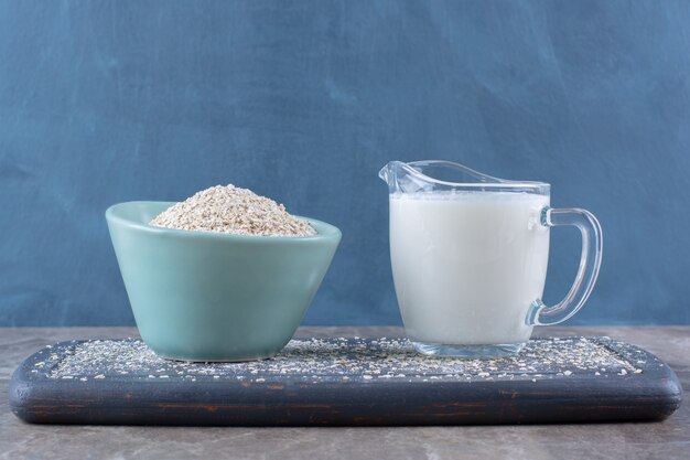 A blue bowl of rice with a glass cup of milk on a wooden board . 