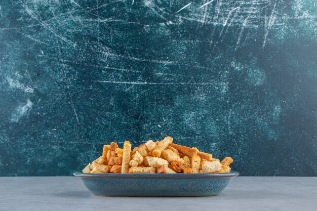 Blue bowl of tasty crispy crackers on stone background.