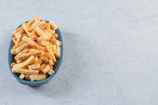 Blue bowl of tasty crispy crackers on stone background.