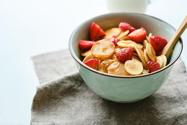 Blue Bowl with cereal tiny pancake with strawberries and maple syrup on a marble board Trendy food concept copy spacexA