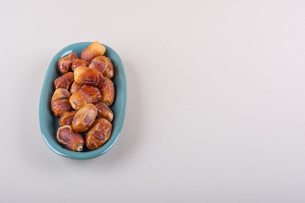 Blue bowl with dried tasty dates on white background. High quality photo