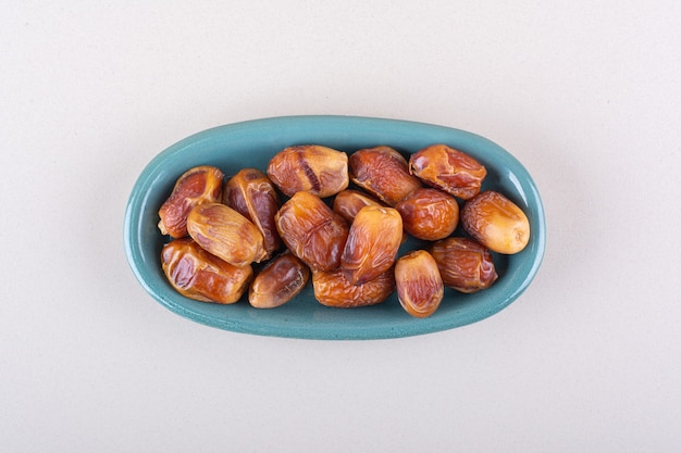 Free photo blue bowl with dried tasty dates on white background. high quality photo