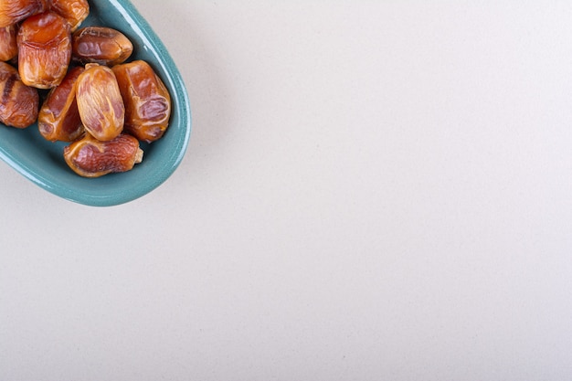 Blue bowl with dried tasty dates on white background. High quality photo