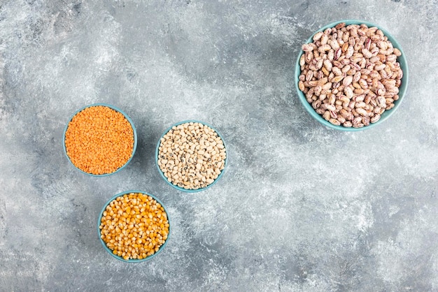 Blue bowls of various beans and corns on marble table.