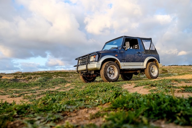 Blue car on the hill covered in the grass under the sunlight and a cloudy sky