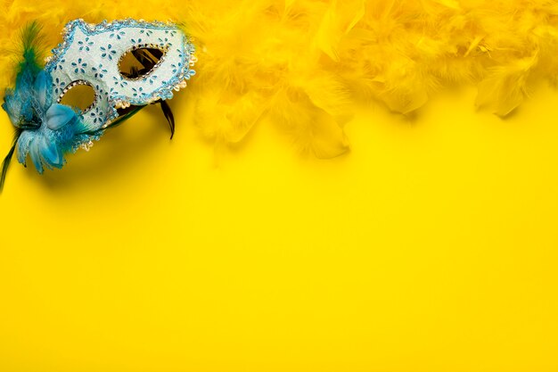 Blue carnival mask with yellow feather boa and copy space