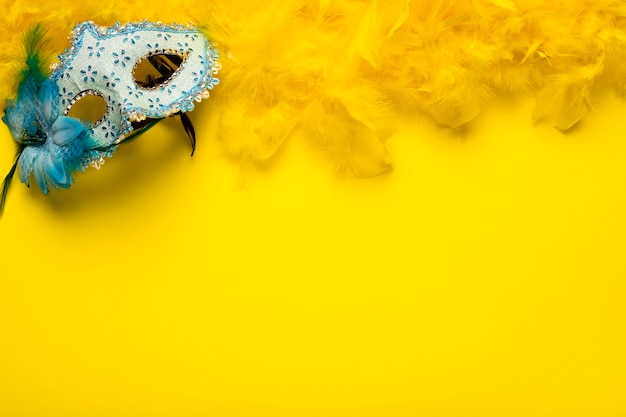 Blue carnival mask with yellow feather boa and copy space