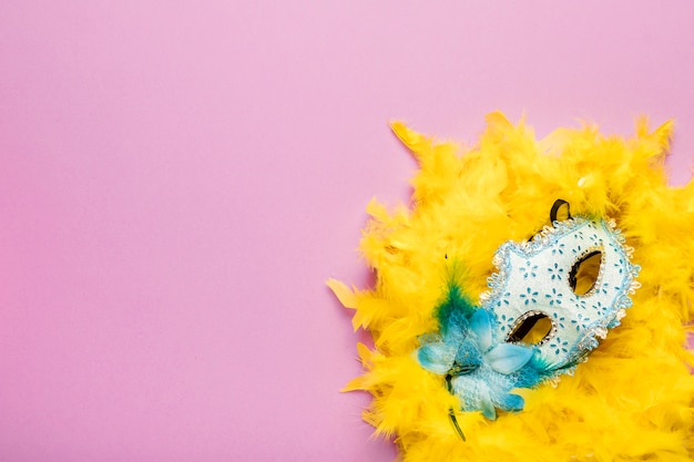 Foto gratuita maschera blu di carnevale con il boa di piuma giallo su fondo rosa con lo spazio della copia