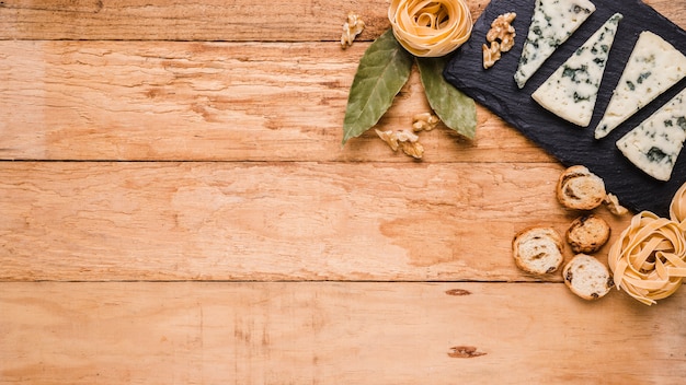 Blue cheese; bread; pasta and bay leaves on black stone over worktop with space for text