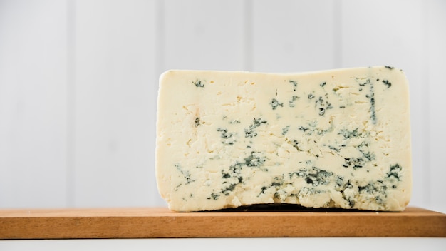 Blue cheese piece on wooden chopping board over white desk