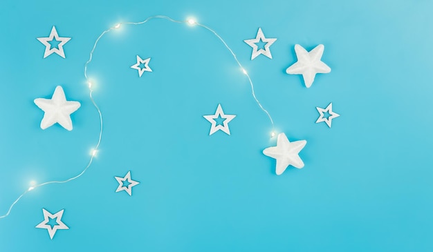 Free photo blue christmas background with garland and decorative stars flat lay