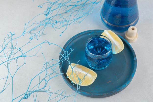 Blue cocktail with lemon slices on blue plate. 