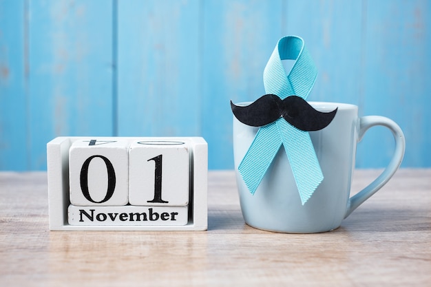 Голубая кофейная чашка, голубая лента, черные усы и календарь на 1 ноября. , отец, международный день мужчин, осведомленность рака простаты