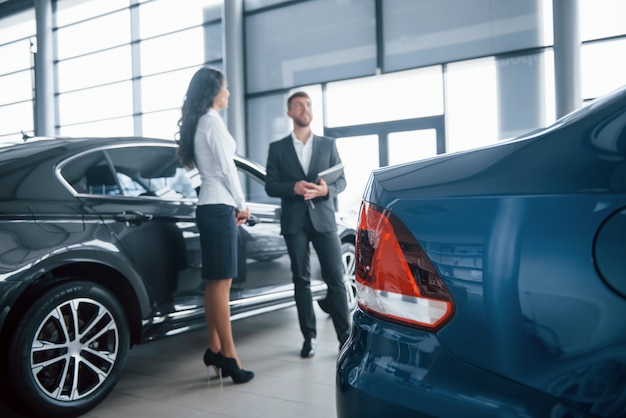 Foto gratuita auto di colore blu. cliente femminile e uomo d'affari barbuto alla moda moderno nel salone dell'automobile