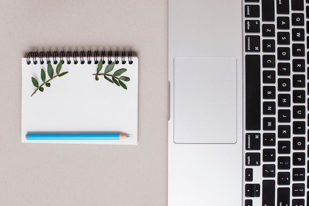 Blue colored pencil on spiral notepad and laptop on gray backdrop