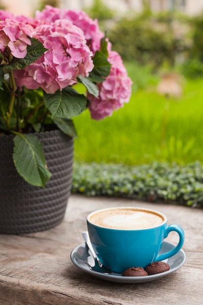 핑크 꽃 냄비 근처 나무 표면에 쿠키와 라 떼 커피의 블루 컵