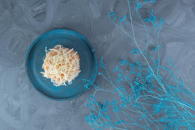 Синие декоративные ветви рядом с блюдом с сырной частью вареного риса на мраморном столе.