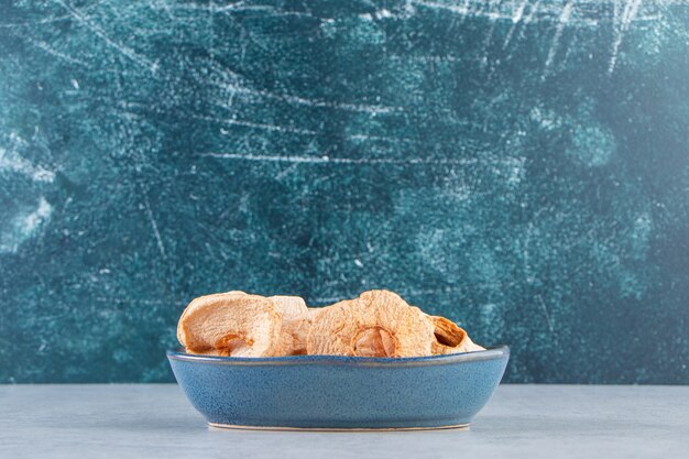 돌 배경에 건강에 좋은 말린 사과가 있는 파란색 깊은 접시.