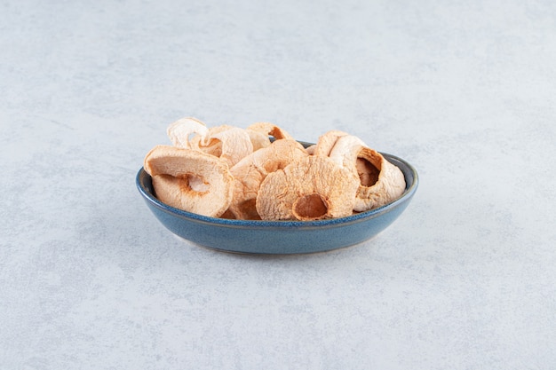 A blue deep plate with healthy dried apples on stone.