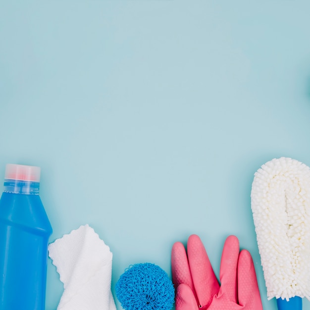 Синяя бутылка моющего средства; салфетка; губка; розовые перчатки на синем фоне