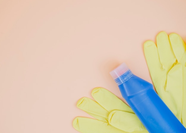 Free photo blue detergent bottle with yellow gloves on peach backdrop