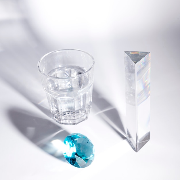 Blue diamond; long crystal and glass of water with shadow on white background