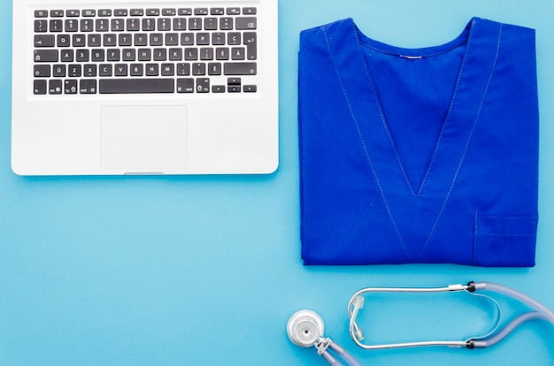 Blue doctor coat; stethoscope and laptop on blue background