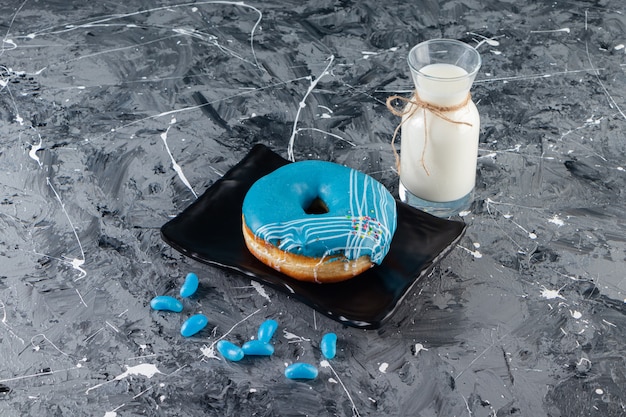 Blue donut with cream frosting and glass of milk on marble table.