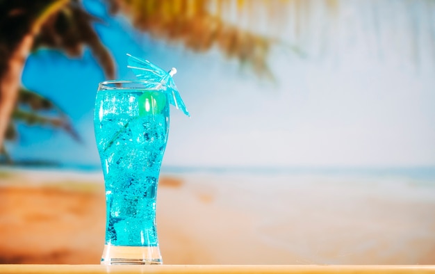 Blue drink with ice cubes in long umbrella decorated glass