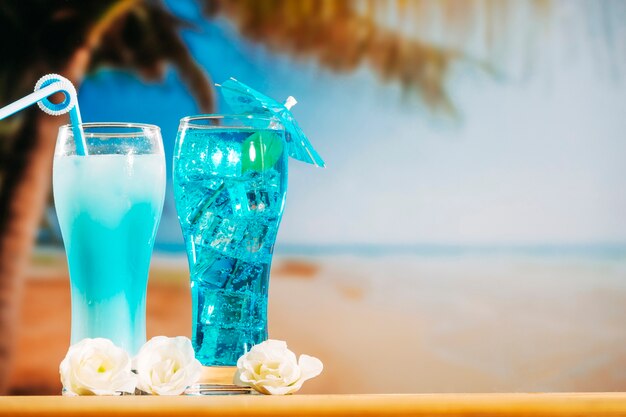 Blue drinks with straw in umbrella decorated glasses and flowers