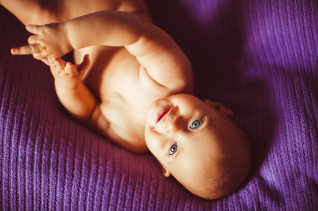 Blue-eyed baby lies on violet blanket
