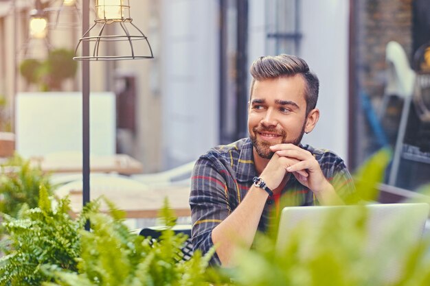 Blue eyed, bearded male using a laptop in a cafe on a street.