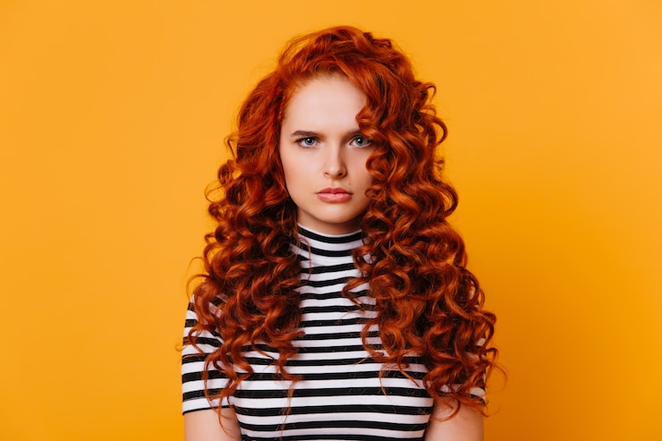 Free Photo blue-eyed curly girl with sad face expression looks into camera. redhead woman in striped top on orange space.