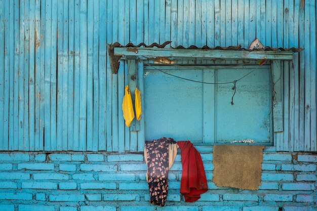 窓に掛けられた服を着た古い木造の郊外の建物の青いファサード