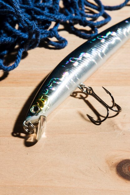 Blue fishing net with silver fishing lure with sharp hook on wooden desk