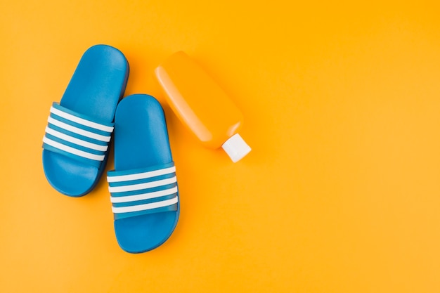 Blue flip-flops with sunscreen lotion bottle on yellow backdrop