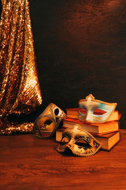 Blue and golden masks with vintage books and glitter sequins textile on wooden desk