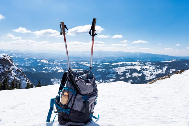 Сине-серый рюкзак с треккинговым снаряжением сбоку на переднем плане покрытых гор
