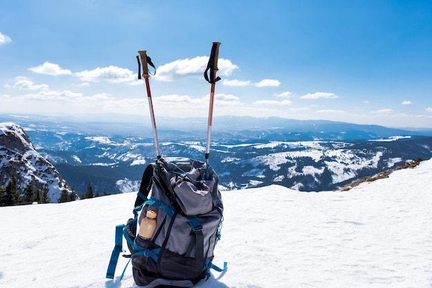 Сине-серый рюкзак с треккинговым снаряжением сбоку на переднем плане покрытых гор