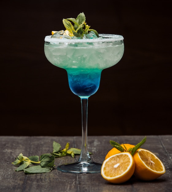 Blue and green cocktail garnished with lemon and mint in long stem glass