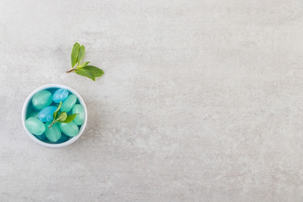Blue and green hard candies in bowl placed on stone table.