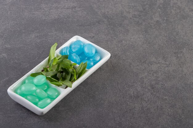 Blue and green hard candies in bowl placed on stone table.