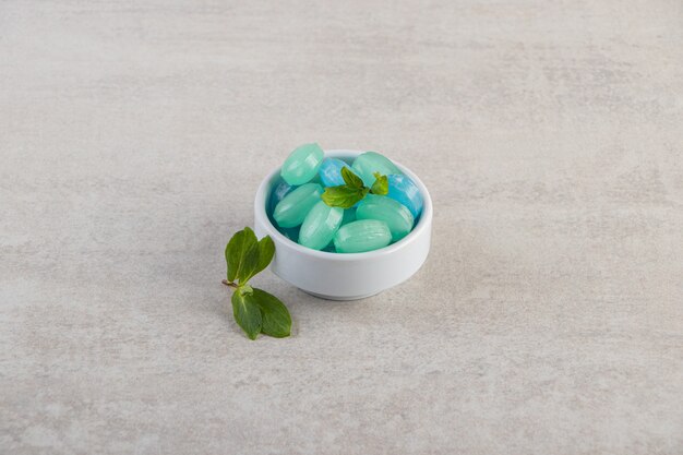 Blue and green hard candies in bowl placed on stone table.