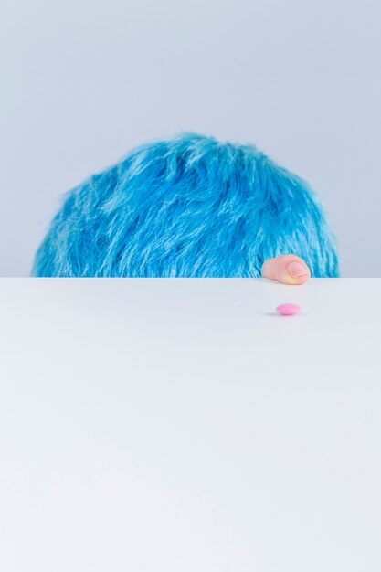 Blue hair head and finger at the edge of table with pink pill