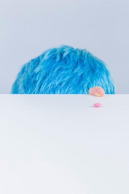 Blue hair head and finger at the edge of table with pink pill