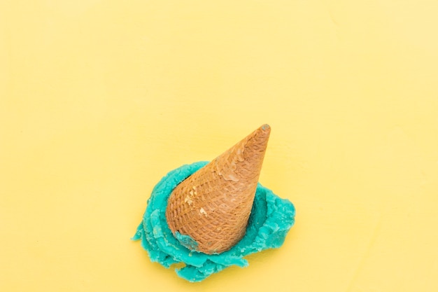 Blue ice cream in cone falling on yellow background