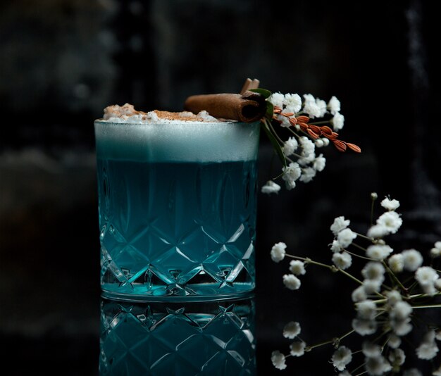 Blue lagoon cocktail glass with white foam and flower decoration 