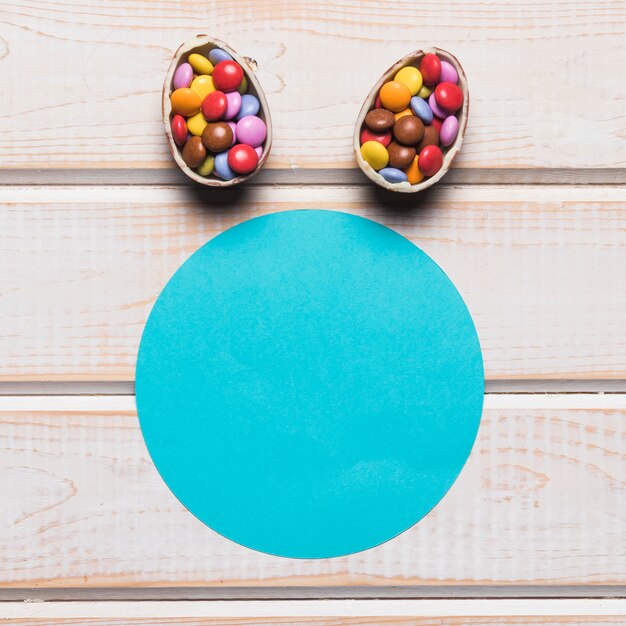 Blue paper circular frame with easter eggs filled with colorful gem candies over the wooden desk