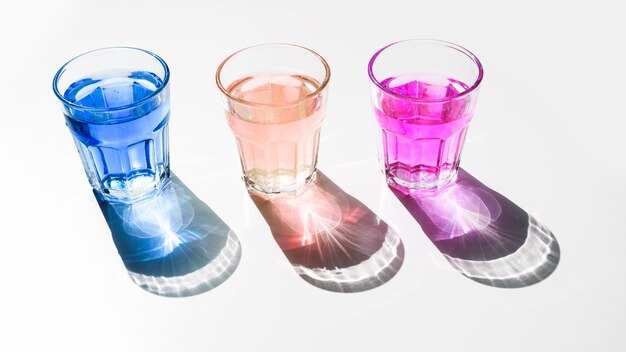 Blue; pink and red liquid glasses with shiny dark shadow on white backdrop